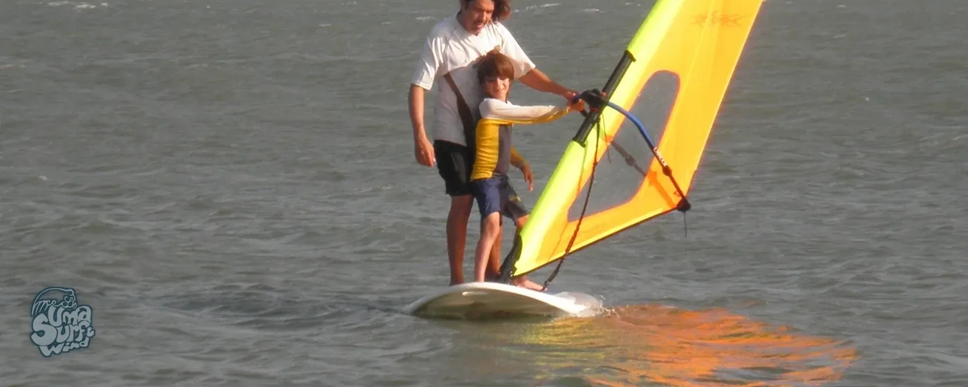 Instructor de Uma enseñando windsurf a un niño sobre la tabla